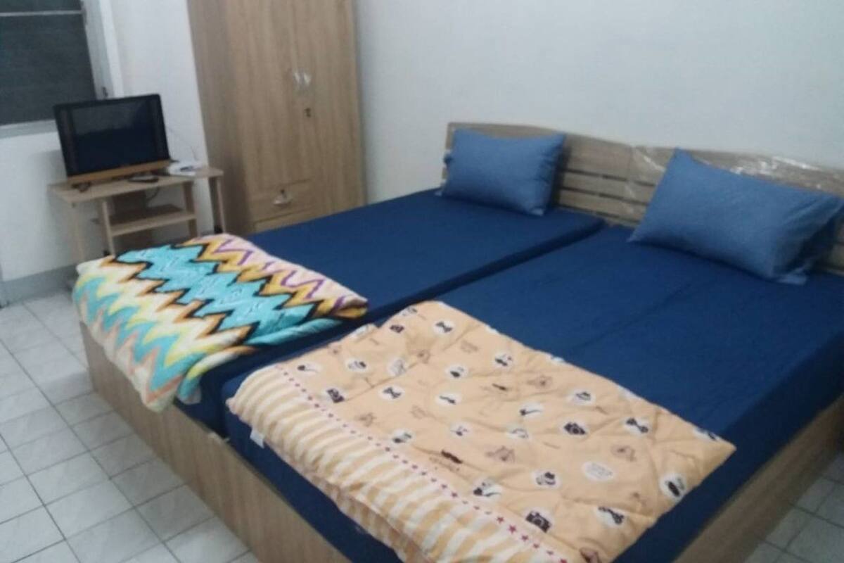 Un dormitorio con cama, televisor sobre un soporte y armario.