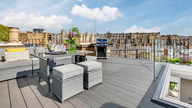 A rooftop terrace with wicker furniture, a table with drinks, and a view of city buildings.