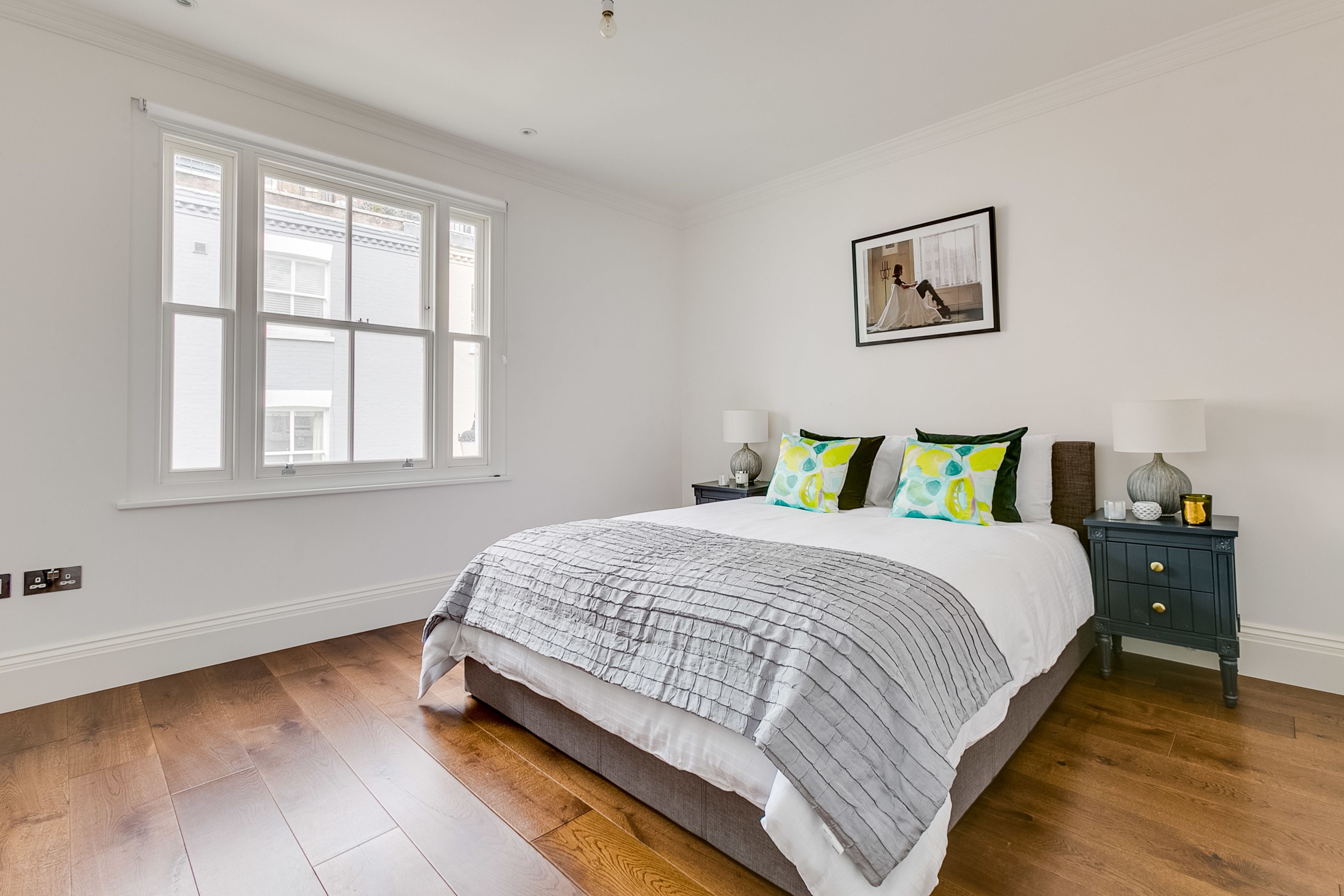 A bedroom with a large bed, a nightstand, a window, and a framed picture on the wall.