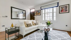 A modern living room with a white sofa, a glass coffee table, and a large mirror.