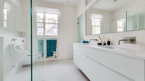 A modern bathroom with a glass partition, a urinal, a sink with a mirror, and a window with a view of buildings.