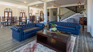 A spacious living room with two blue sofas, a glass coffee table, and a staircase leading to an upper floor. - The Wind Castle (Nuwara Eliya)