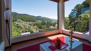 A room with large windows offering a view of a green valley and distant mountains. - The Wind Castle (Nuwara Eliya)