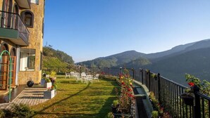 A terrace with a view of mountains, a stone building, and outdoor furniture. - The Wind Castle (Nuwara Eliya)