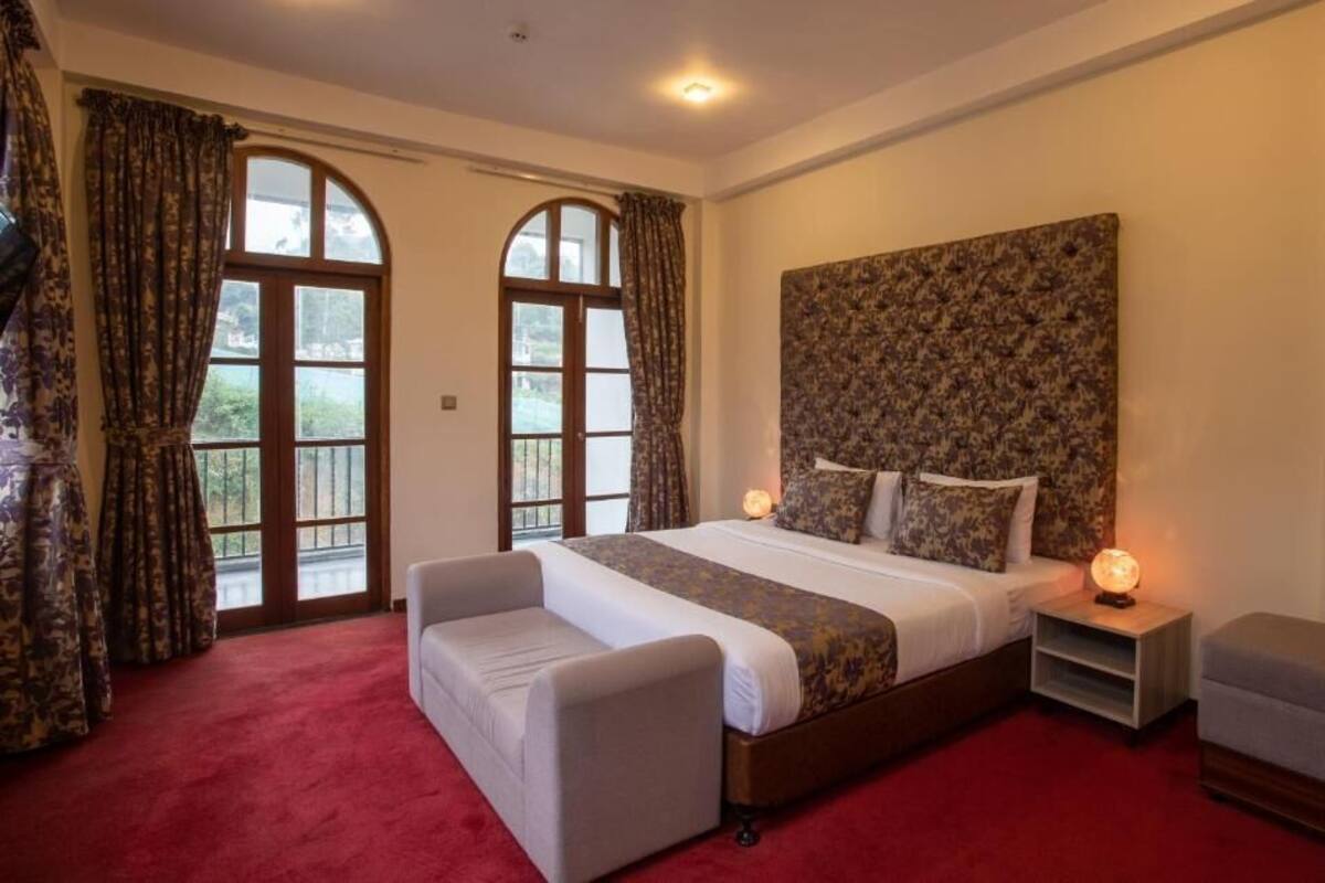 A bedroom with a large bed, two bedside tables, a nightstand, and a window with curtains.