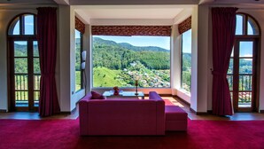 A room with a large window offering a view of a mountainous landscape. There is a pink sofa and a small table with a lamp. - The Wind Castle (Nuwara Eliya)