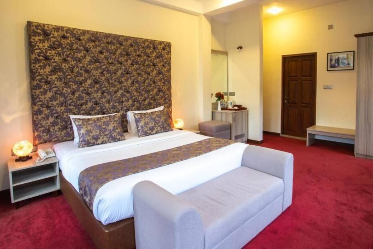 A bedroom with a large bed, a bedside table with a lamp, a small table with a vase, a wardrobe, and a bench.