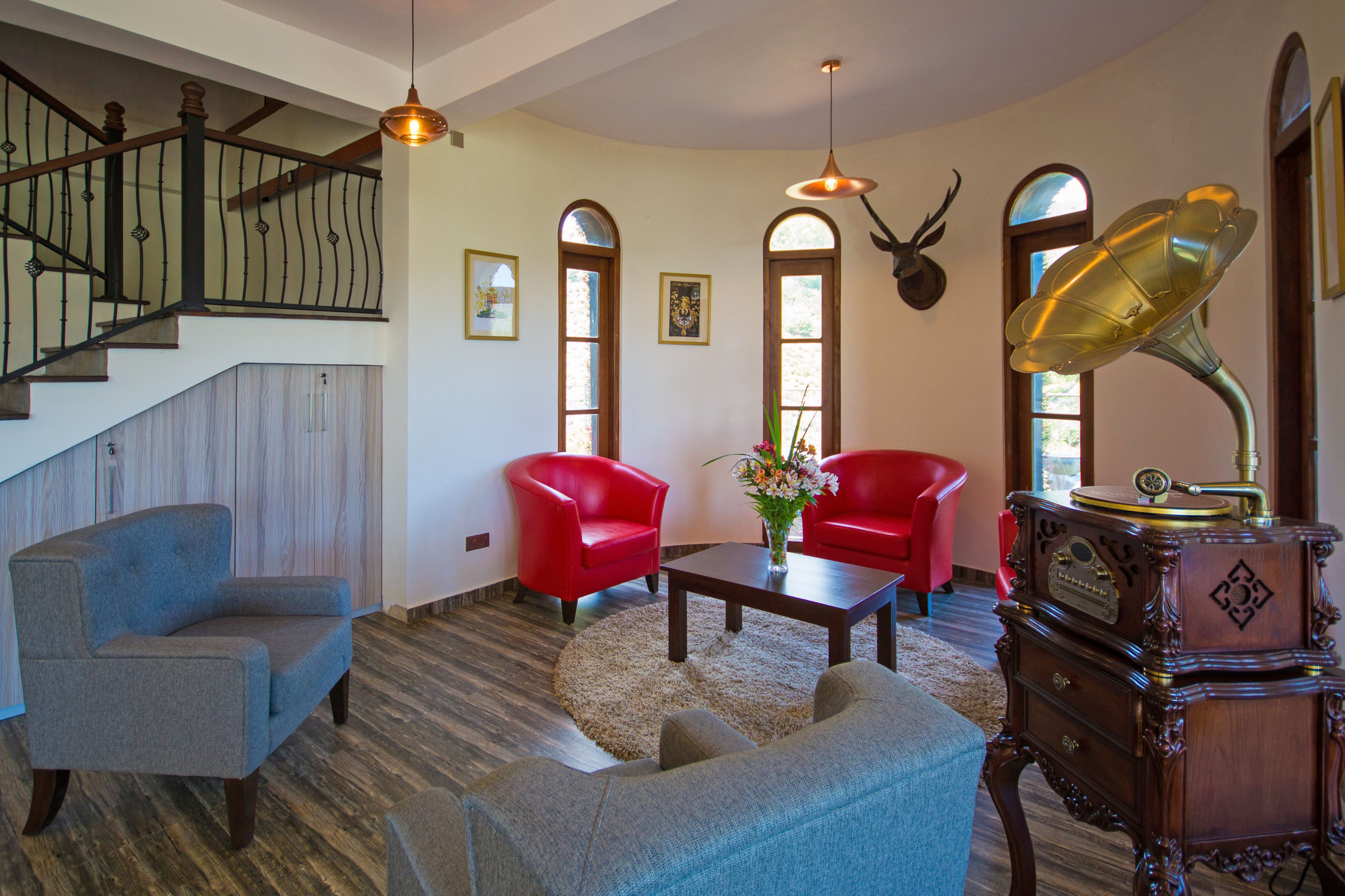 A spacious living room with a staircase, red chairs, a coffee table, and a gramophone.