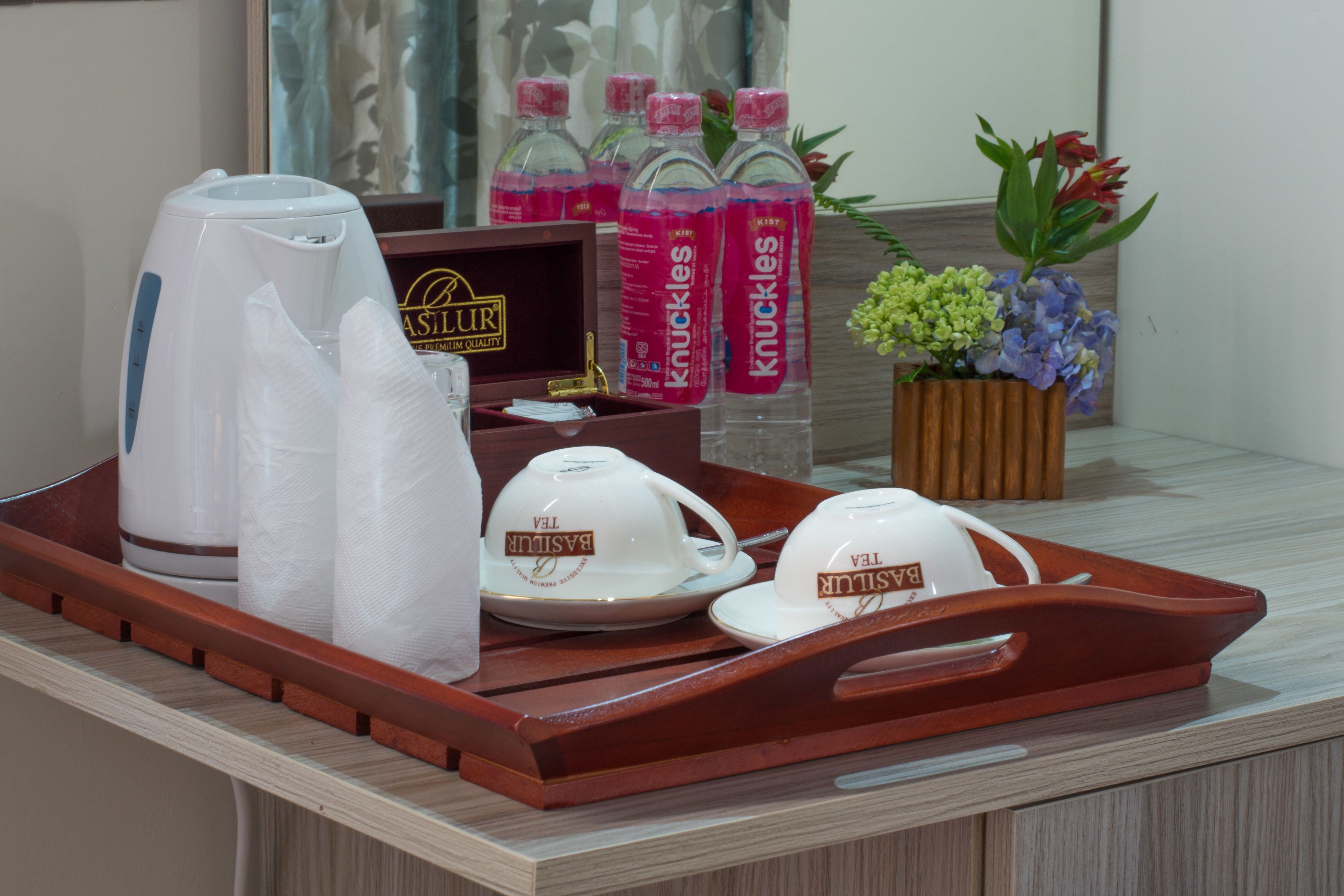 A tray with a coffee maker, napkins, and tea cups, along with bottles of Knuckles water and a flower arrangement.