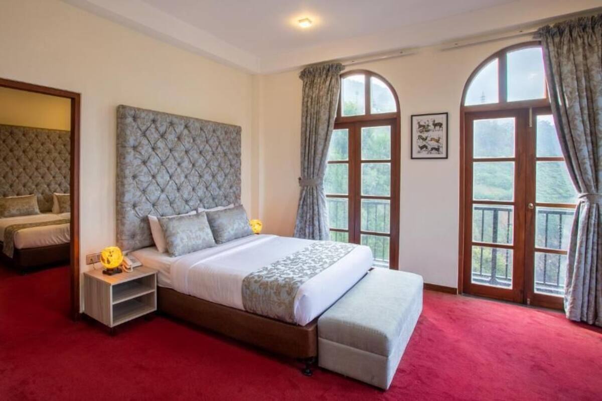 A bedroom with a large bed, a nightstand, a red carpet, and a window with curtains.