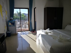 Ein Hotelzimmer mit Bett, Kleiderschrank, Schreibtisch mit Stuhl, Mülleimer und Blick auf den Außenbalkon.
