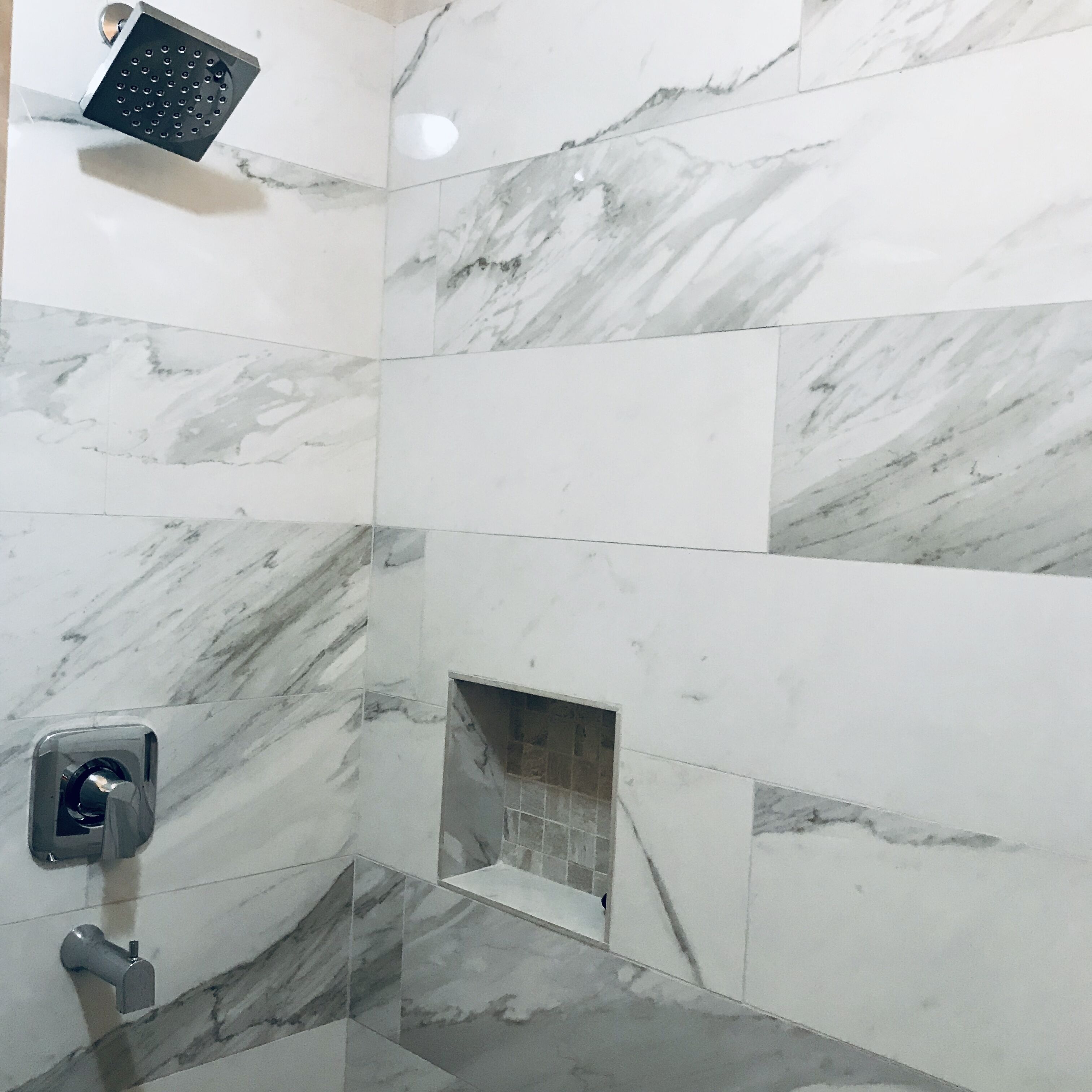 Un baño con baldosas de mármol blanco, un cabezal de ducha y un secador de manos.