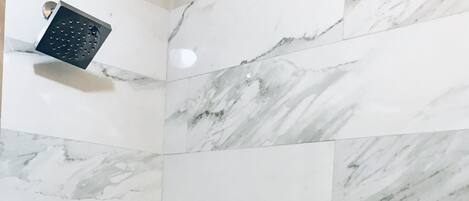 Un baño con baldosas de mármol blanco, un cabezal de ducha y un secador de manos.