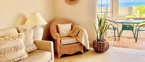 A living room with a sofa, a wicker chair, a table, and a potted plant.