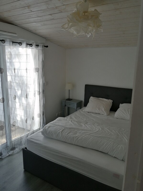 Un dormitorio con cama, mesita de noche, lámpara y cortinas translúcidas con estampado floral.