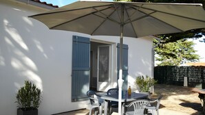 Een terras met een tafel, stoelen, een plant in pot en een grote parasol.