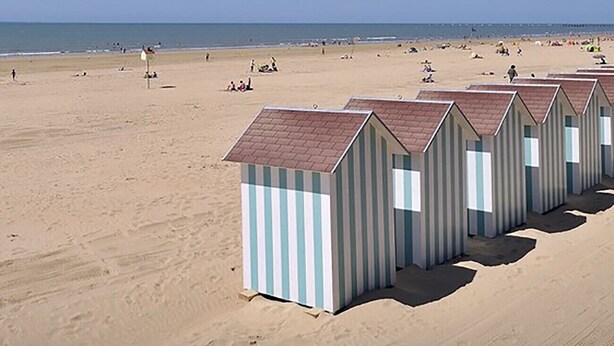 Strandhutten met gestreepte muren en rode daken, rijend in het zand geplaatst.