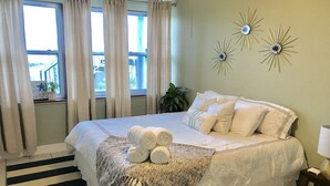 A neatly made bed with white linens and rolled towels, a striped rug, and decorative wall art. - Waterfront, Dog Friendly, Bring your boat + family beach and dock! (Pensacola Beach)