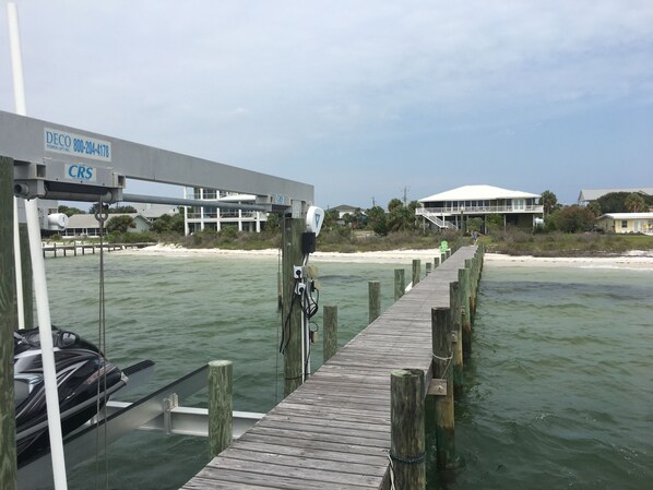 A wooden pier leading to a dock with a boat and a building in the background. - Waterfront, Dog Friendly, Bring your boat + family beach and dock! (Pensacola Beach)