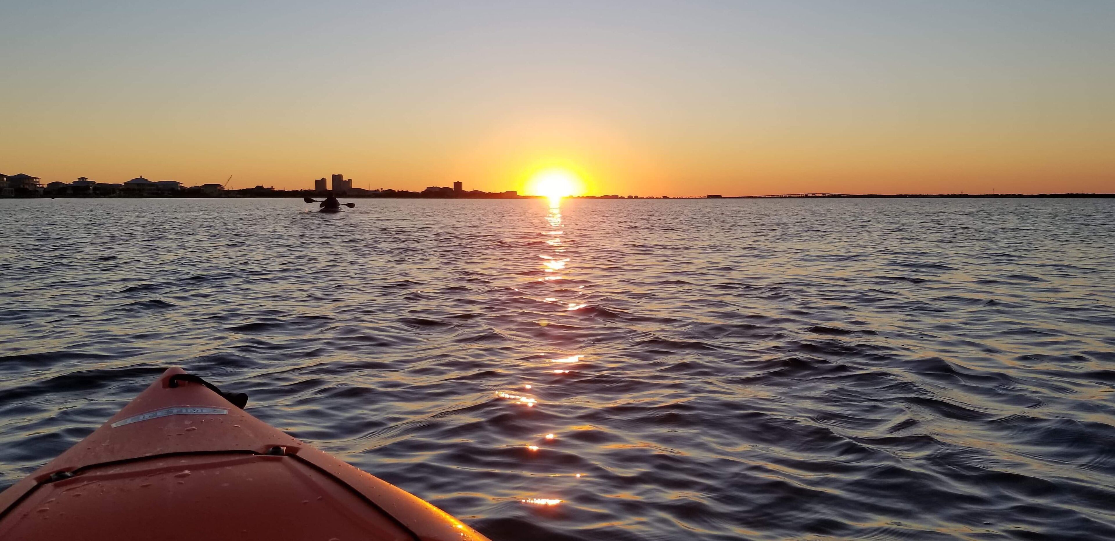 Un kayak sobre aguas tranquilas con un atardecer de fondo.