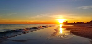 Una spiaggia con un tramonto, onde e edifici in lontananza.