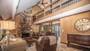 A spacious living area with a stone fireplace, a high ceiling with a fan, and a large wall clock. - McKinney Cove by Hauserman Rentals (Homewood)