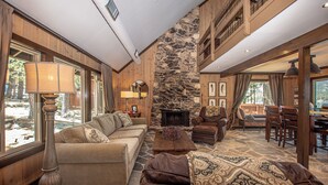 A spacious living area with a stone fireplace, wooden furniture, and large windows. - McKinney Cove by Hauserman Rentals (Homewood)