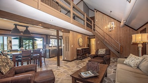 A spacious interior with a dining area, a living room with a sofa and armchairs, a staircase, and a view through large windows. - McKinney Cove by Hauserman Rentals (Homewood)