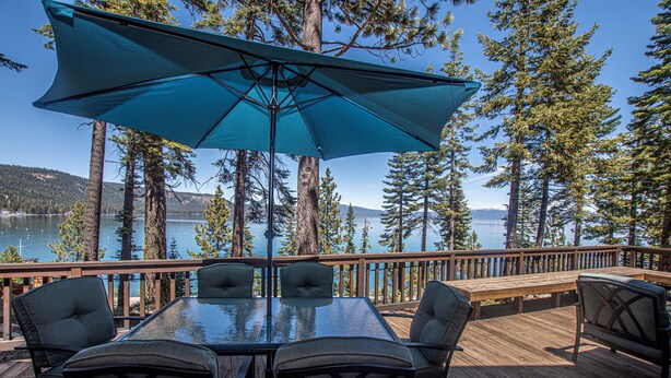 A deck with a glass-top table and chairs, surrounded by tall trees and overlooking a body of water. - McKinney Cove by Hauserman Rentals (Homewood)