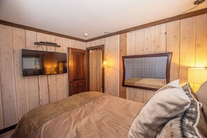 A bedroom with wooden paneling, a bed, a television mounted on the wall, and a door. - McKinney Cove by Hauserman Rentals (Homewood)