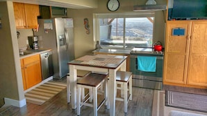 A kitchen with wooden cabinets, stainless steel appliances, a dining table with benches, and a window with a view. - 3 bedrm Luxurious Apartment with Best View in Salt lake City and Private Hot Tub (Draper)