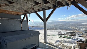 A covered outdoor seating area with a hot tub, a table, and chairs, overlooking a snowy landscape with mountains in the distance. - 3 bedrm Luxurious Apartment with Best View in Salt lake City and Private Hot Tub (Draper)
