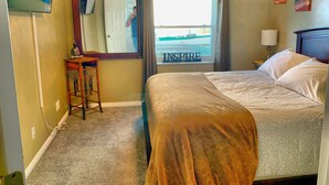 A hotel room with a bed, a desk, a mirror, a window with curtains, and artwork on the wall. - 3 bedrm Luxurious Apartment with Best View in Salt lake City and Private Hot Tub (Draper)