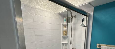 Una ducha con puerta de cristal, paredes de azulejos blancos y una pared de acento azul, además de un perchero para toallas.
