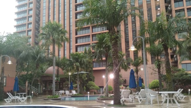 A hotel pool area with lounge chairs and umbrellas, surrounded by palm trees and a high-rise building in the background. - Time Square By Trivaa (Kuala Lumpur)