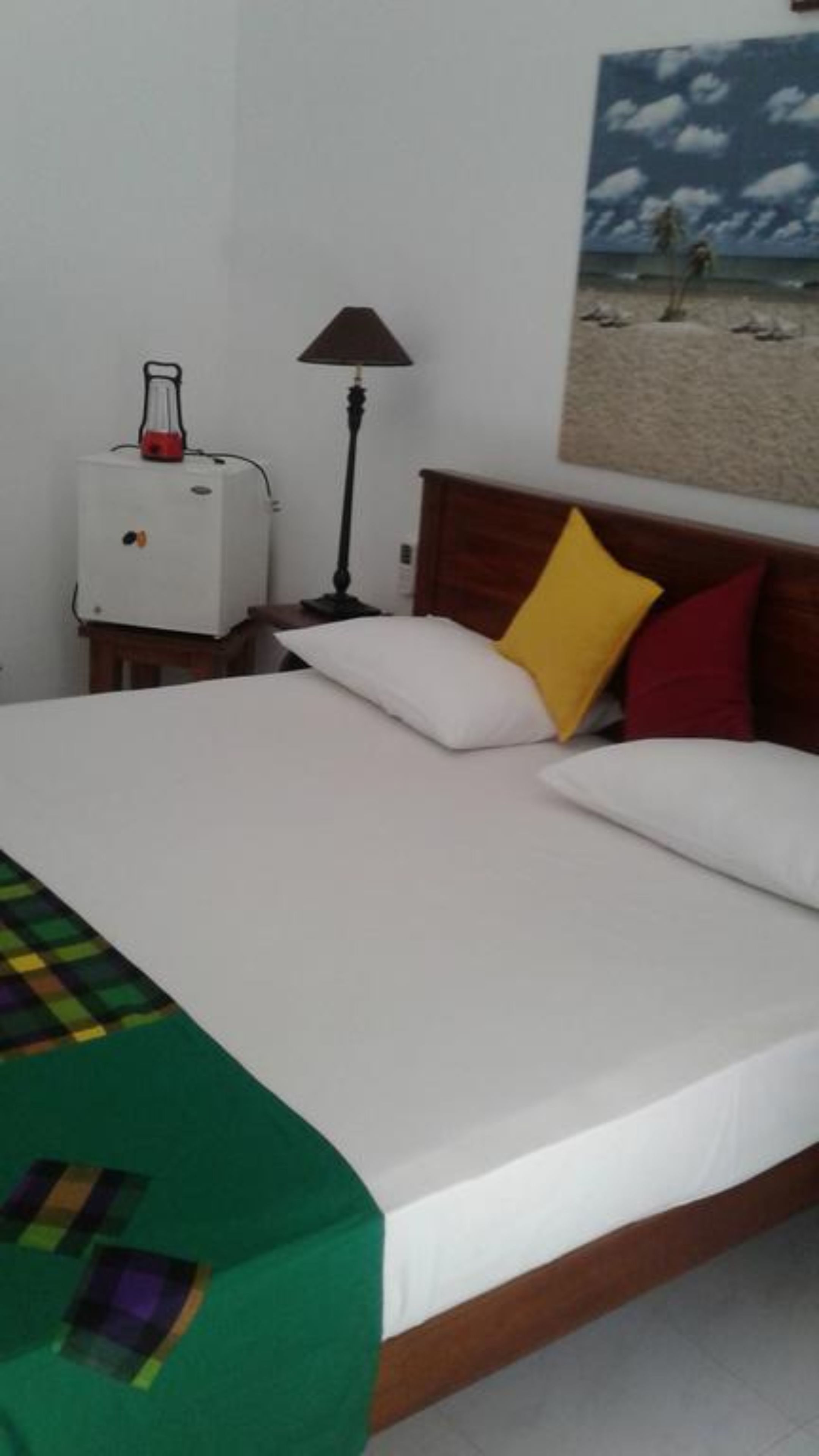 A hotel room with a bed, a nightstand, a lamp, and a painting on the wall.