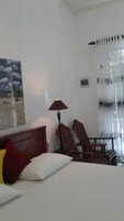 Habitación de hotel con cama, escritorio, silla, lámpara, un cuadro y ventana con cortinas.