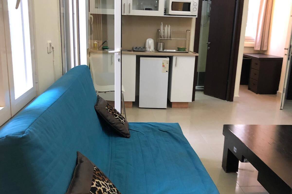 A room with a blue sofa, a small refrigerator, white cabinets, and a microwave.