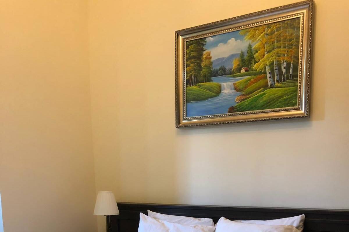 A hotel room with a bed, a painting of a landscape, and a lamp.