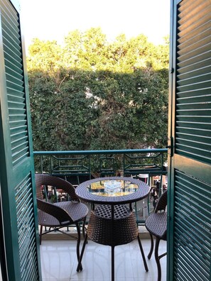 Un balcón con sillas de mimbre y una mesa de vidrio, con vistas a una zona verde exuberante.