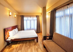 Une chambre d’hôtel avec un lit en bois, un canapé et une fenêtre avec des rideaux.