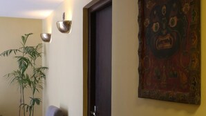 Een kamer met een houten vloer, een donkere deur, een stoel, een potplant en een wandlamp.