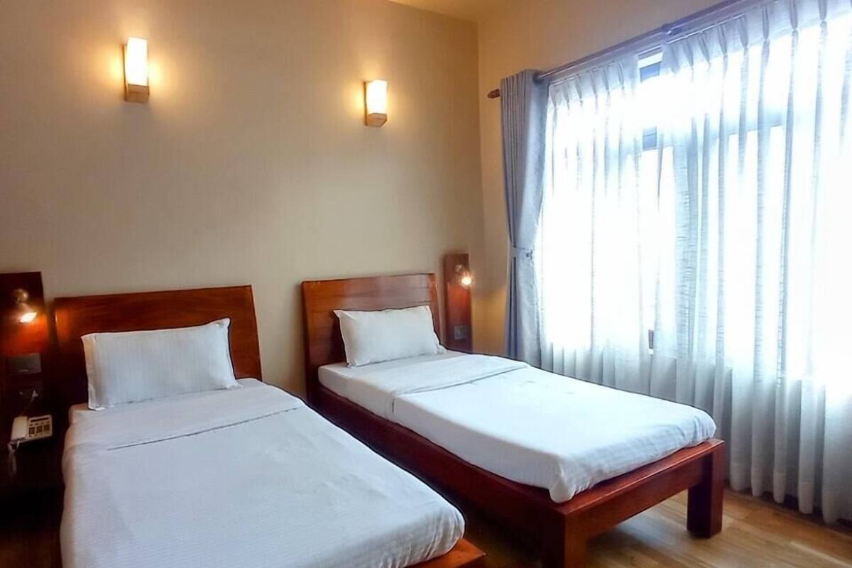 Une chambre d’hôtel avec deux lits en bois, du linge de lit blanc et deux lampes fixées au mur.