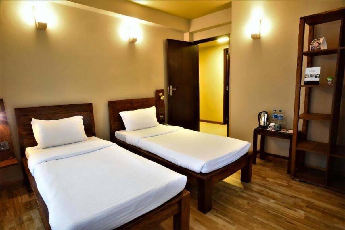 Une chambre d’hôtel avec deux lits simples, des têtes de lit en bois, une petite table de chevet avec une bouteille d’eau et une bibliothèque en bois.