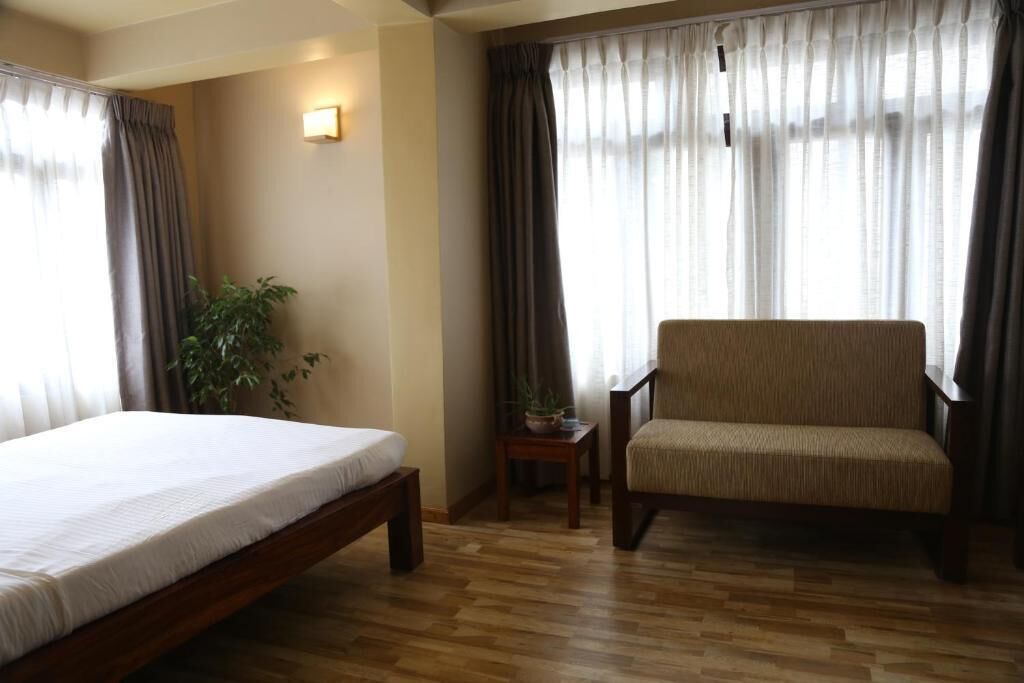 Una habitación de hotel con cama, una silla, una mesita con una planta y cortinas.