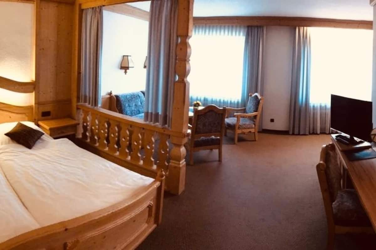 A hotel room with a large bed, a desk, a chair, and a view of the outdoors.