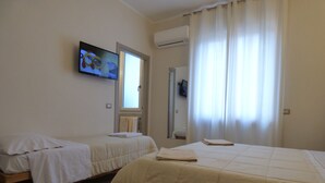 A hotel room with two beds, a television on the wall, and a window with curtains. - Anania (Cagliari)
