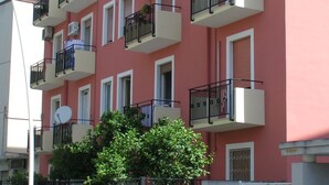 A multi-story building with balconies, a gated entrance, and a tree in front. - Anania (Cagliari)