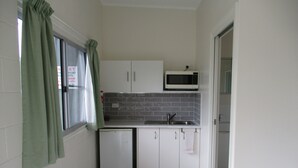 A compact kitchen with white cabinets, a microwave, and a small refrigerator. - Ingham Tourist Park (Ingham)
