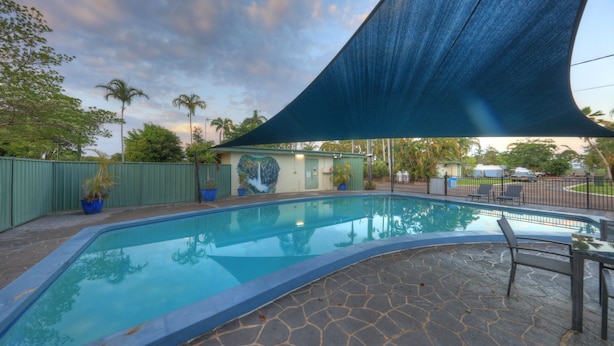 A swimming pool with a stone deck, surrounded by a green fence and potted plants. - Ingham Tourist Park (Ingham)